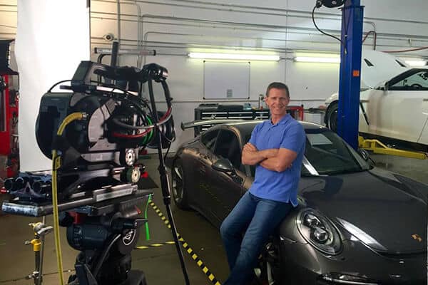 Camera filming man leaning on porsche in mechanic garage for commercial