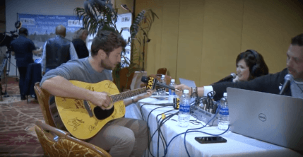 Brett Eldridge playing guitar at table with man holding microphone to him